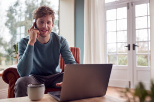 Man Working From Home Using Laptop And Mobile Phone