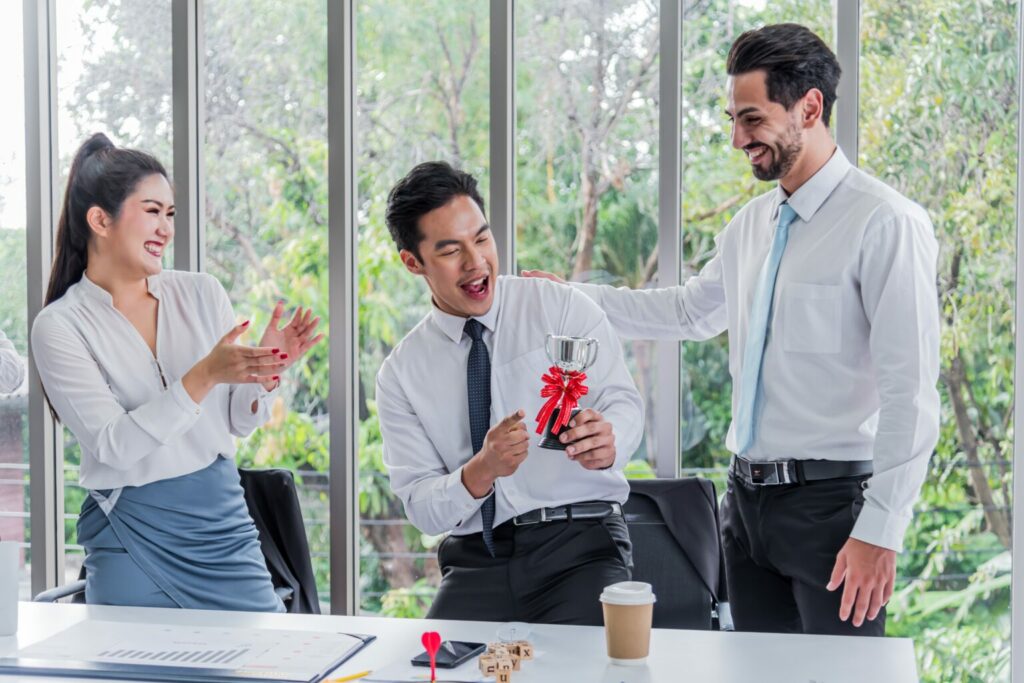 Boss presents an award to an employee for great work and coworker celebrates