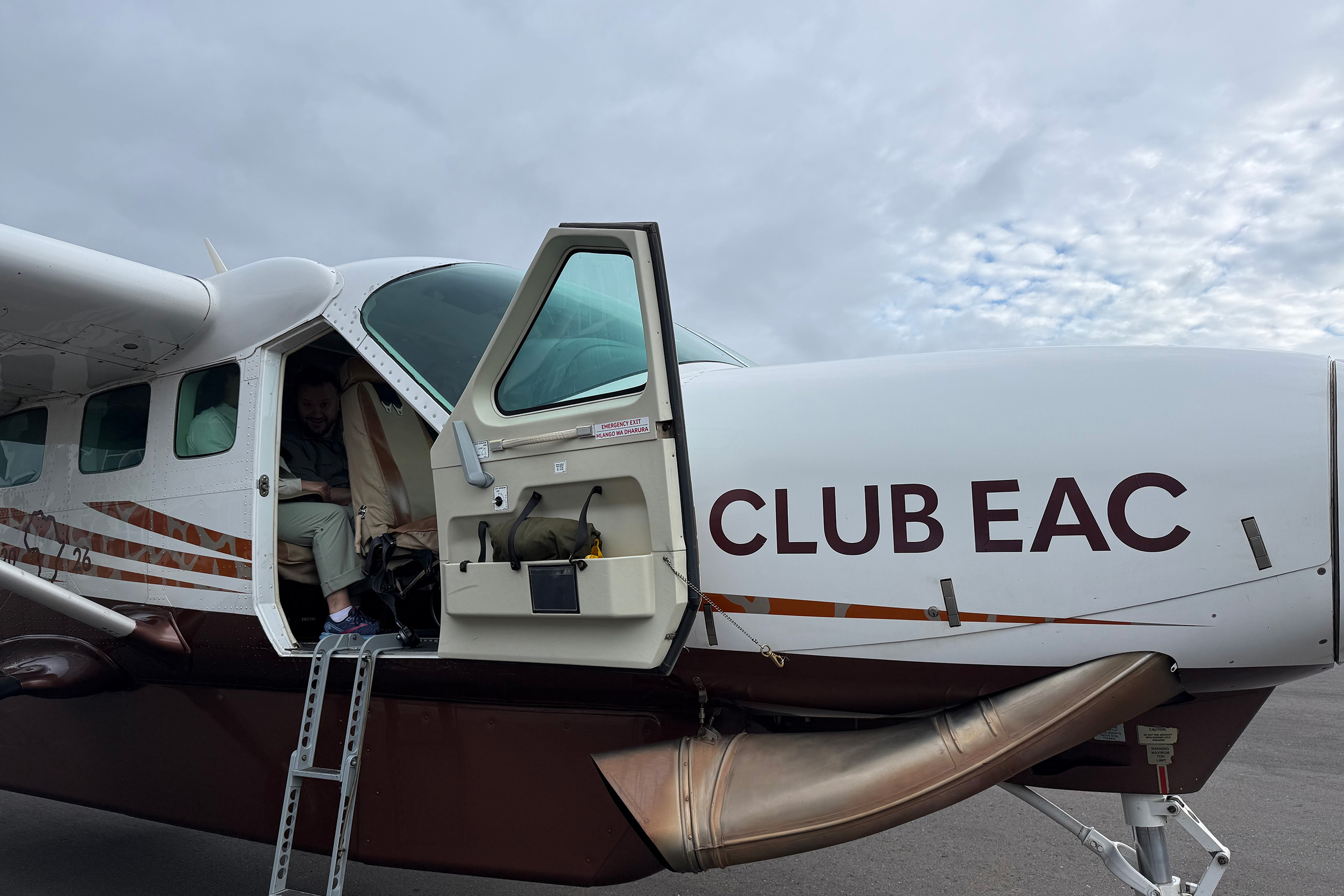 A small propeller airplane with CLUB EAC written on the side is parked on the tarmac, ready for an exciting incentive trip Africa adventure. The cabin door is open, and a person is partially visible inside the doorway, preparing for departure.