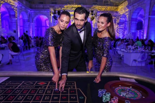 Three well-dressed people stand at a casino roulette table, placing bets with chips, in a large, upscale venue with purple lighting—a thrilling scene perfect for Portugal incentive travel experiences.