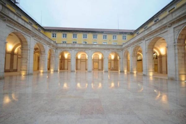 A large, empty marble courtyard with arched walkways and illuminated columns, ideal for Portugal incentive travel, surrounded by a yellow building with multiple windows.