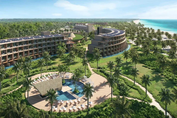 Aerial view of one of the top all-inclusive resorts in Mexico and the Caribbean, featuring modern beachfront buildings, swaying palm trees, a central pool with lounge chairs, and the sparkling ocean in the background.