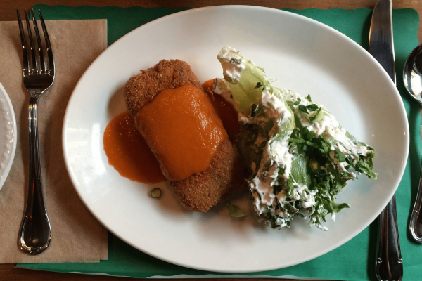 nourriture_01 A plated meal with breaded meat topped with orange sauce and a leafy salad with creamy dressing, set beside a fork, knife, and spoon—a perfect dining experience during Incentive Travel to Québec City.